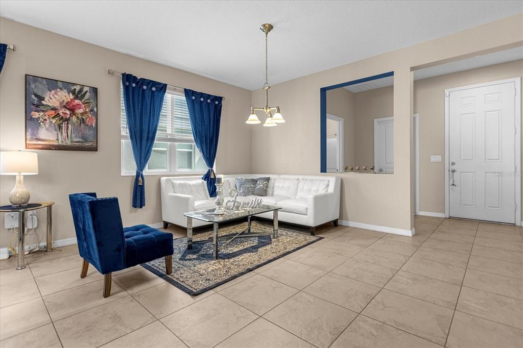A living room features a white sofa, blue accent chair, tile flooring, and a front door — 8060 BOWERY DRIVE, WINTER GARDEN, FL