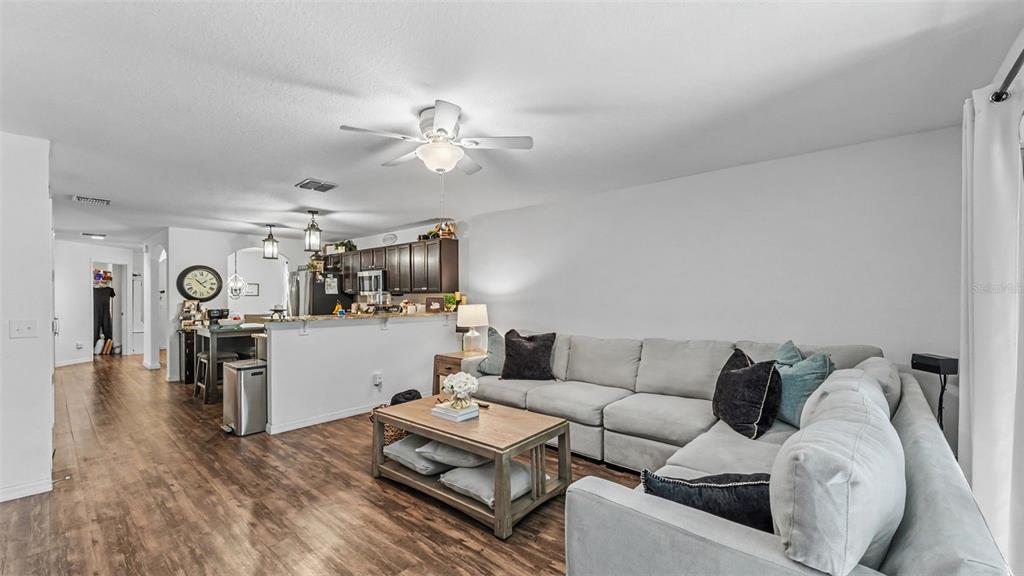 A living room with a sectional sofa and coffee table opens to a kitchen area — 6270 MANITOBA DRIVE, LAKELAND, FL