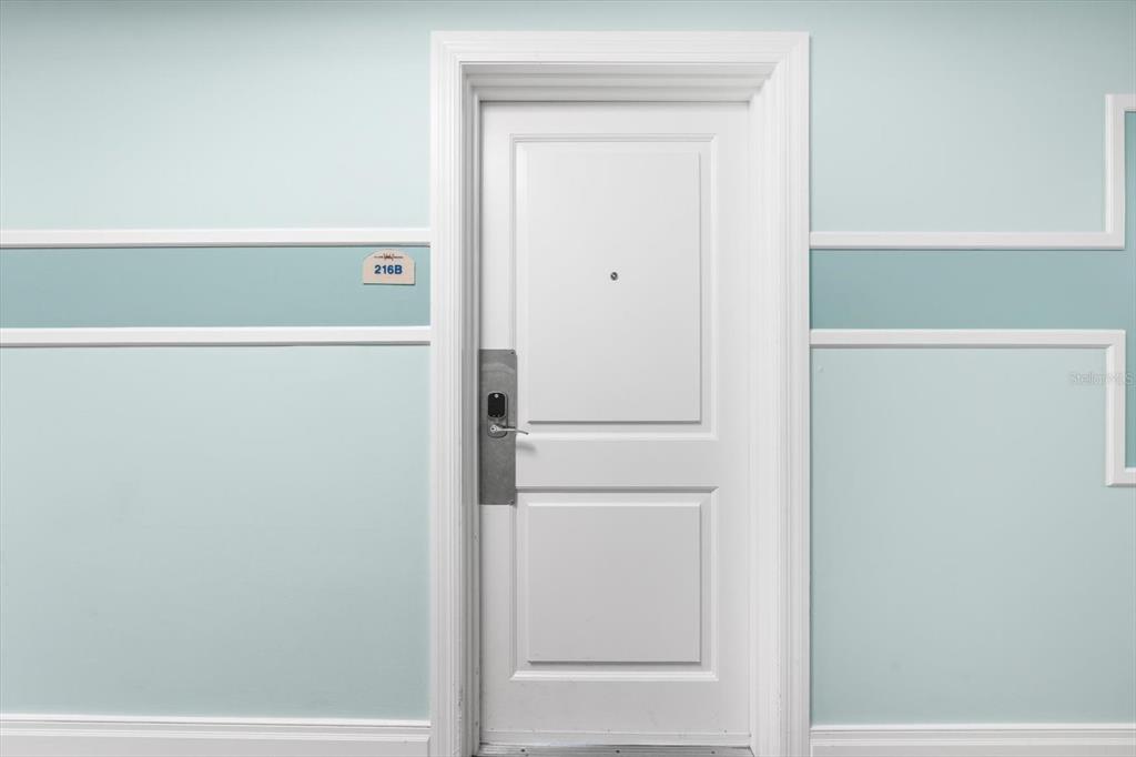 A white door with a silver electronic lock is centered on a light blue wall — 536 BAHIA BEACH BOULEVARD UNIT 216B, RUSKIN, FL