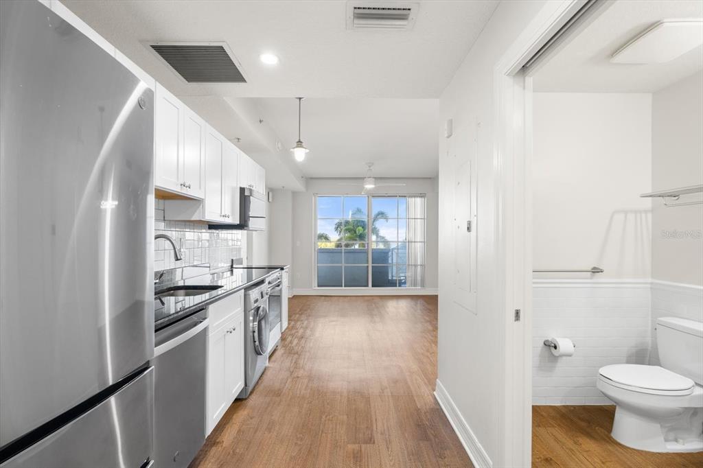 A kitchen with stainless steel appliances and white cabinets opens to a living area — 536 BAHIA BEACH BOULEVARD UNIT 216B, RUSKIN, FL