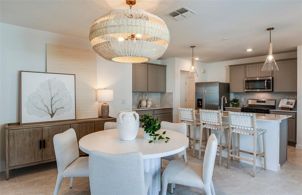 A dining area with a round table and a kitchen featuring gray cabinets and stools — 1391 ALLAGASH DRIVE, ZEPHYRHILLS, FL