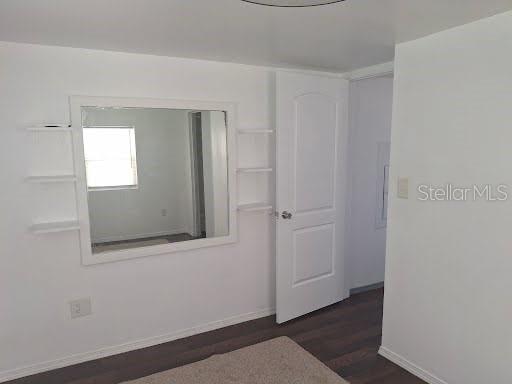 A room with white walls, dark wood flooring, a large wall mirror, and a white door — 9723 TOM STREET, HUDSON, FL