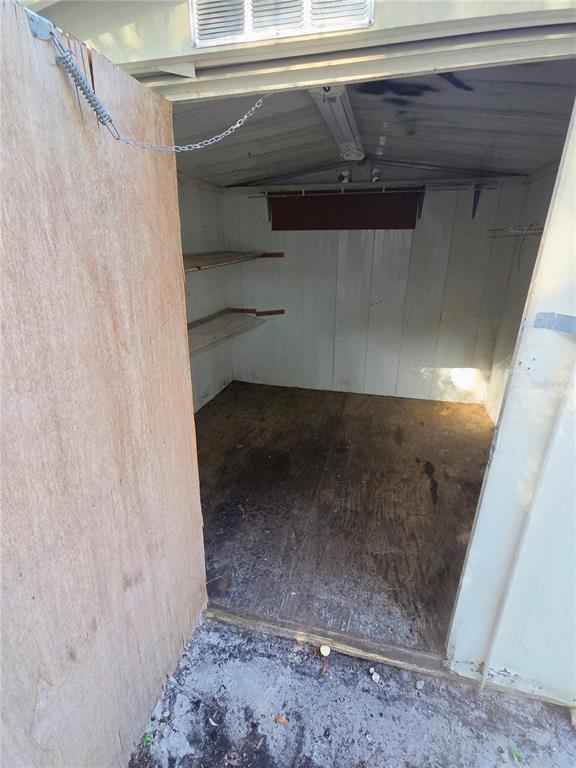 An open door reveals the interior of a small, empty storage shed with wooden shelving — 3000 CLARCONA ROAD UNIT 244, APOPKA, FL