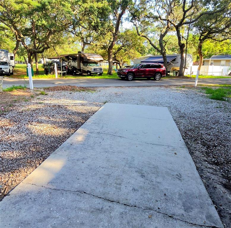 A concrete driveway leads toward a gravel road with parked vehicles and mature trees — 3000 CLARCONA ROAD UNIT 244, APOPKA, FL