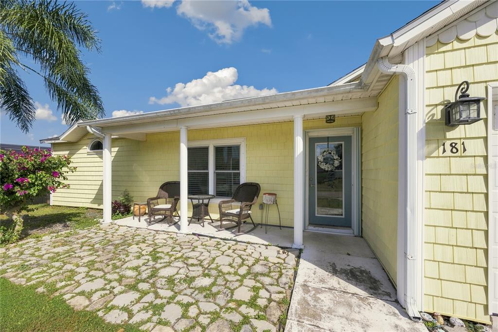 A yellow house exterior features a stone patio, a covered porch, and a blue front door — 181 HAMMOCK ROAD SE, PALM BAY, FL