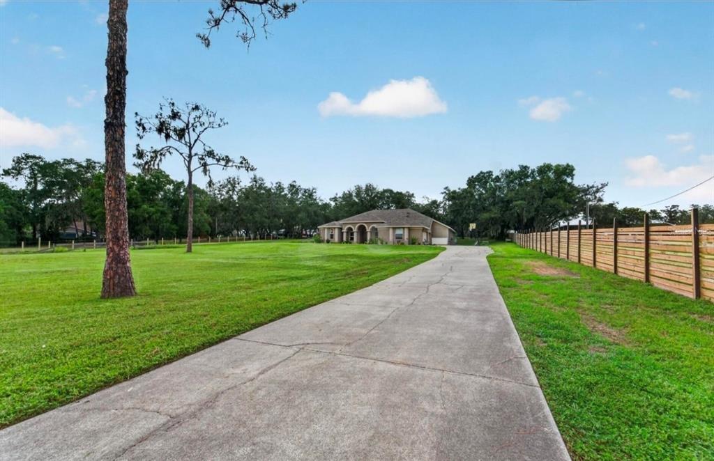 A long concrete driveway leads to a single-story house situated on a large grassy lot — 13020 SHADOW RUN BOULEVARD, RIVERVIEW, FL
