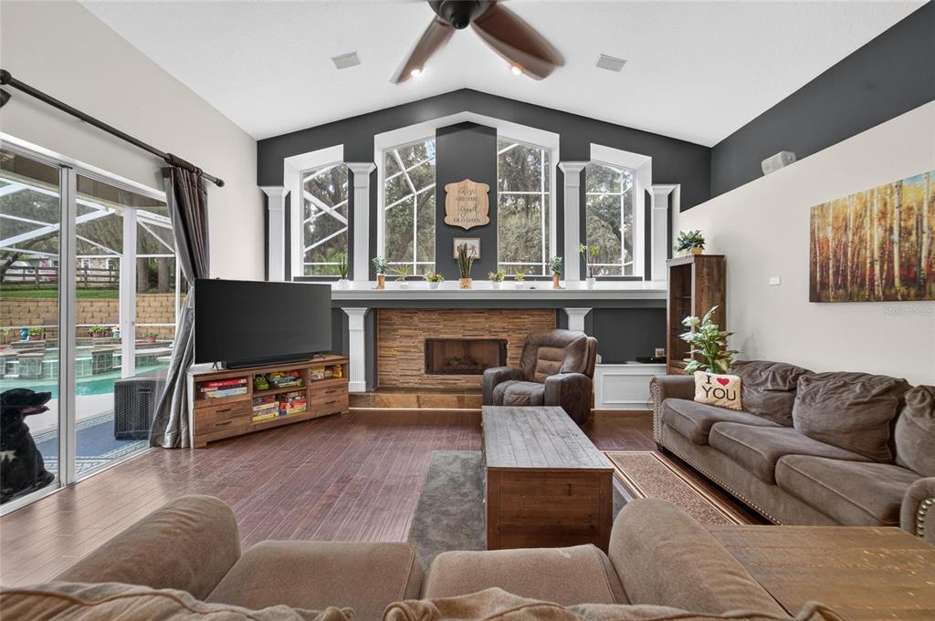 A living room features a stone fireplace, large windows, wood flooring, and a sliding glass door — 13020 SHADOW RUN BOULEVARD, RIVERVIEW, FL