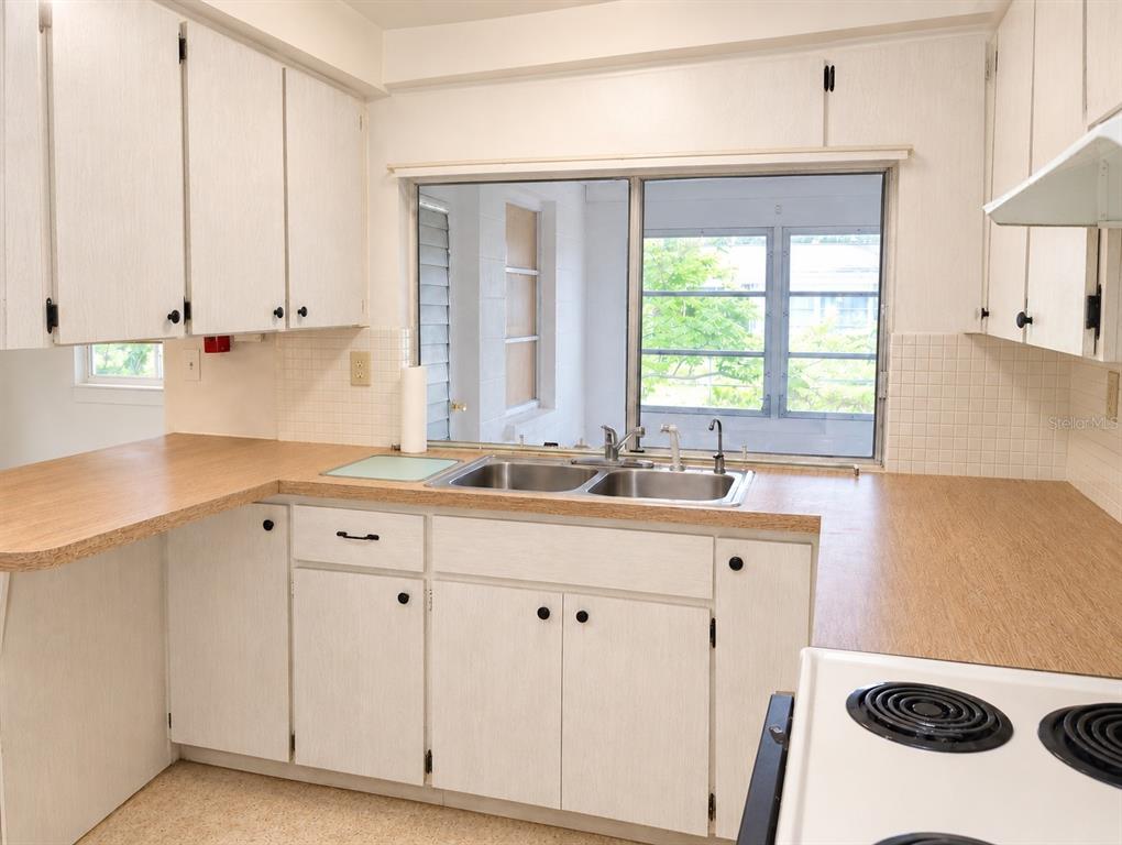 A kitchen features white cabinets, wood-look laminate countertops, a double-basin sink, and a large window — 3519 BROOKSTON DRIVE, HOLIDAY, FL