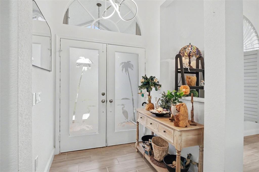An entryway features double doors with palm tree frosted glass and a wooden console table — 301 GOLD TREE, PUNTA GORDA, FL