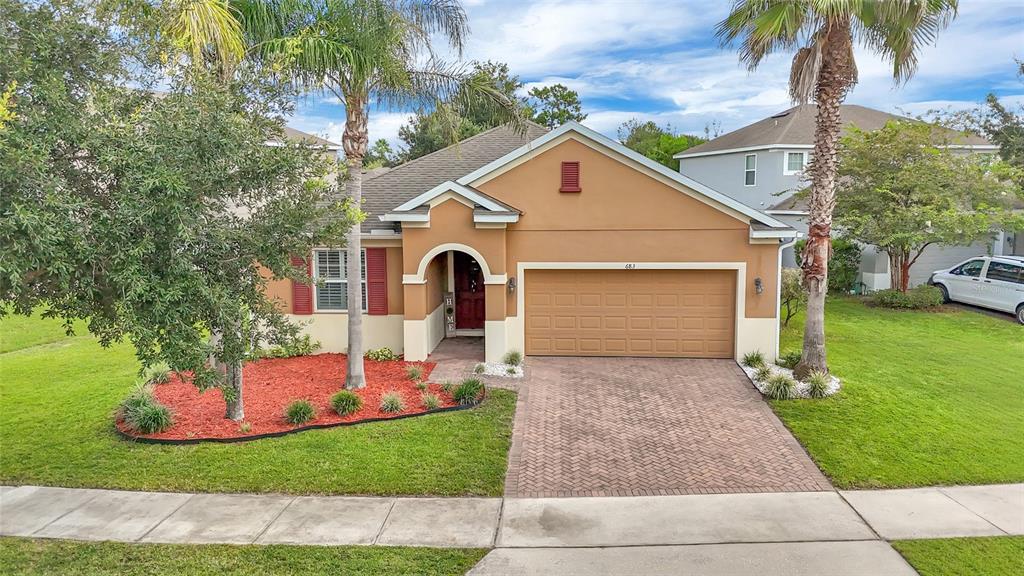 A single-story house with a tan stucco exterior, red shutters, and a brick-paved driveway — 683 CHAMPIONS GATE BOULEVARD, DELAND, FL