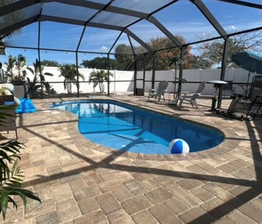 A screened-in patio features a swimming pool surrounded by stone pavers and a teal house — 1002 SILVER PALM WAY, APOLLO BEACH, FL