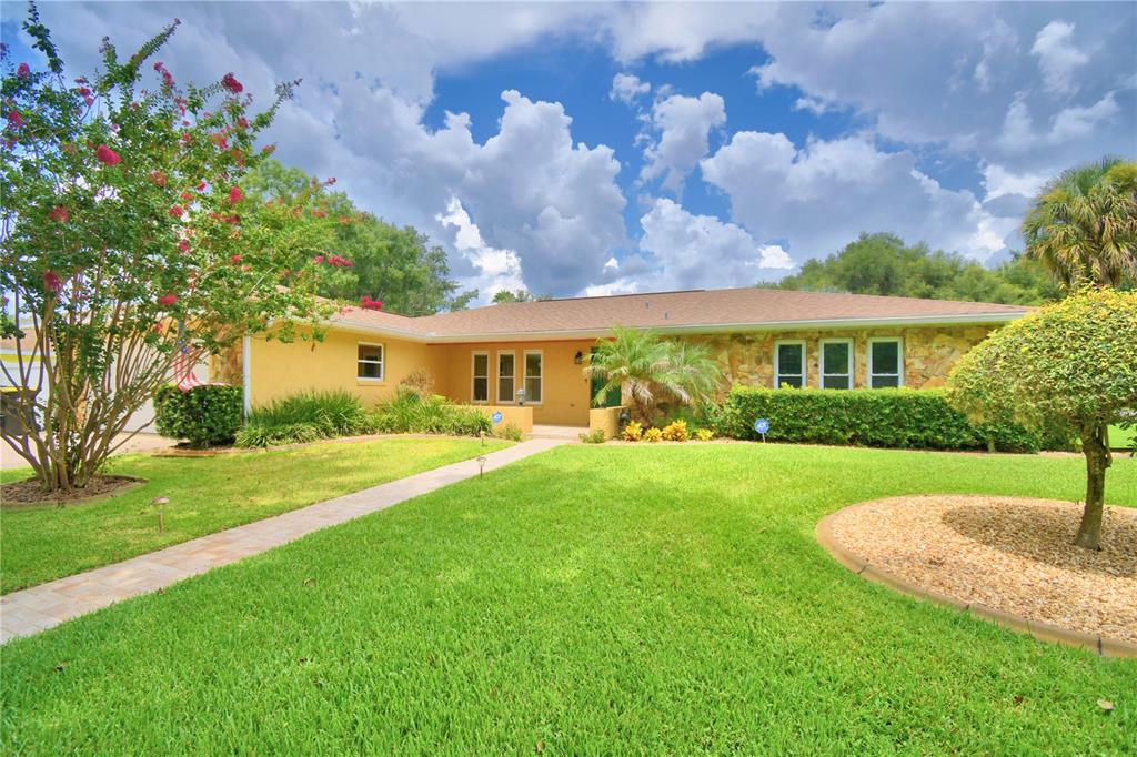 A single-story house with a white garage, stone accents, and a large tree in front — 902 CRESTVIEW DRIVE, AUBURNDALE, FL