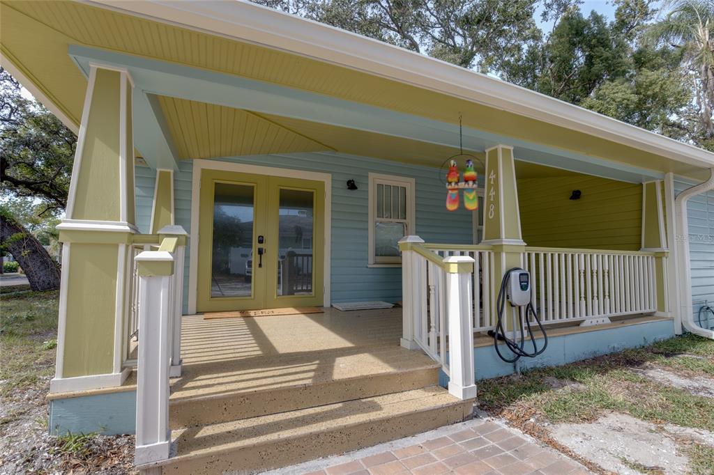 A covered front porch features light blue siding, green trim, and an electric vehicle charger — 448 LOCKLIE STREET, DUNEDIN, FL