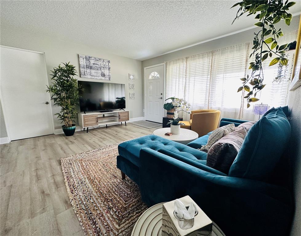 A living room features a blue velvet sectional, a television on a console, and wood-look flooring — 1886 CLEMATIS LANE, WINTER PARK, FL