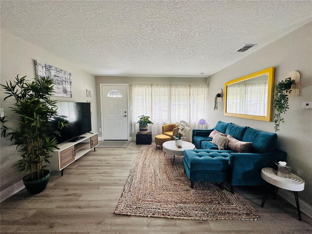 A living room features a blue sectional sofa, a television, and light wood-look flooring — 1886 CLEMATIS LANE, WINTER PARK, FL