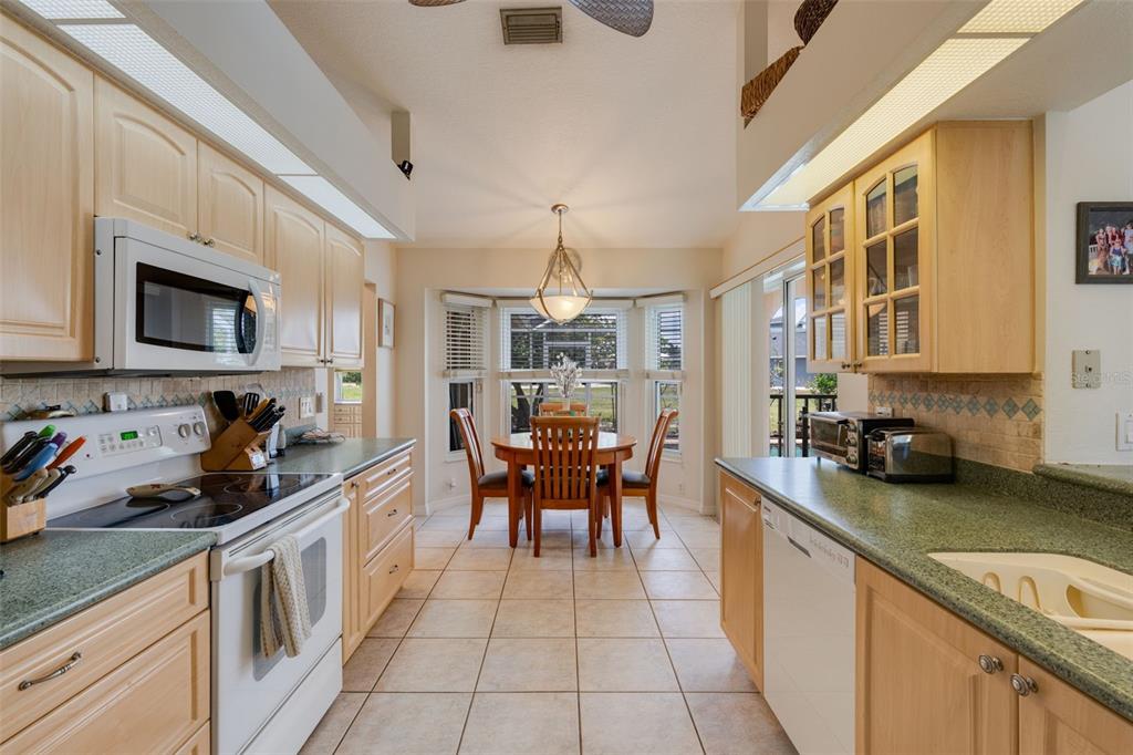A kitchen with light wood cabinets, green countertops, and a dining area with a bay window — 154 ACALYPHA, PUNTA GORDA, FL