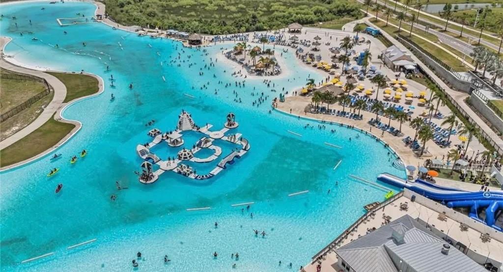 An aerial view shows a large swimming lagoon with an inflatable obstacle course and water slides — 8358 HARDY BAY LOOP, WESLEY CHAPEL, FL