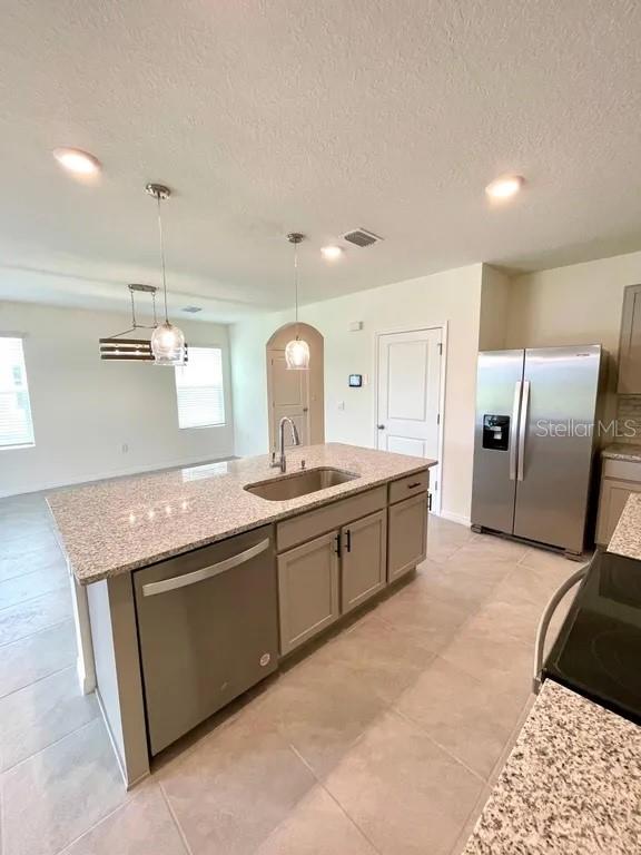 A kitchen island with a granite countertop and stainless steel dishwasher sits before a refrigerator — 8358 HARDY BAY LOOP, WESLEY CHAPEL, FL