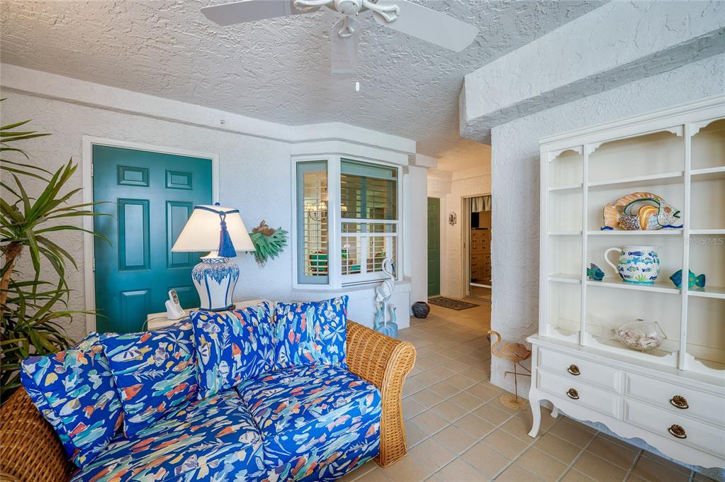 A sunroom features a wicker sofa with blue patterned cushions, a white hutch, and tile flooring — 4565 S ATLANTIC AVENUE UNIT 5308, PONCE INLET, FL