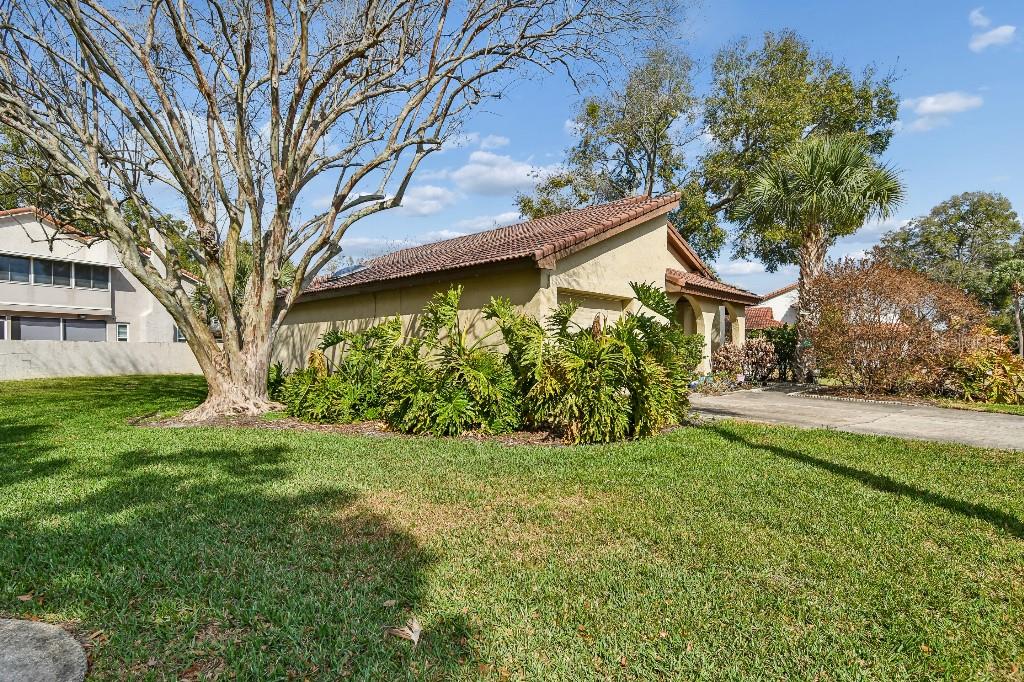 A tan house with a tiled roof sits behind large green shrubs and a bare tree — 6609 EDGEWORTH DRIVE, ORLANDO, FL