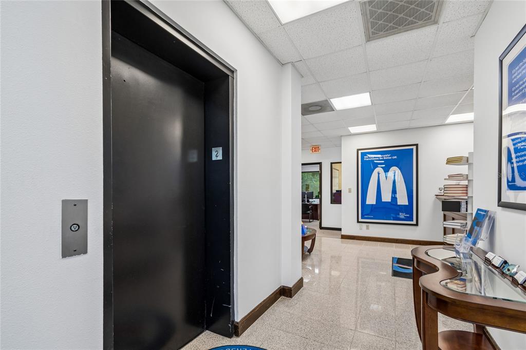 A hallway features a black elevator door, white walls, a tiled floor, and framed wall art — 1301 66TH STREET N, ST PETERSBURG, FL