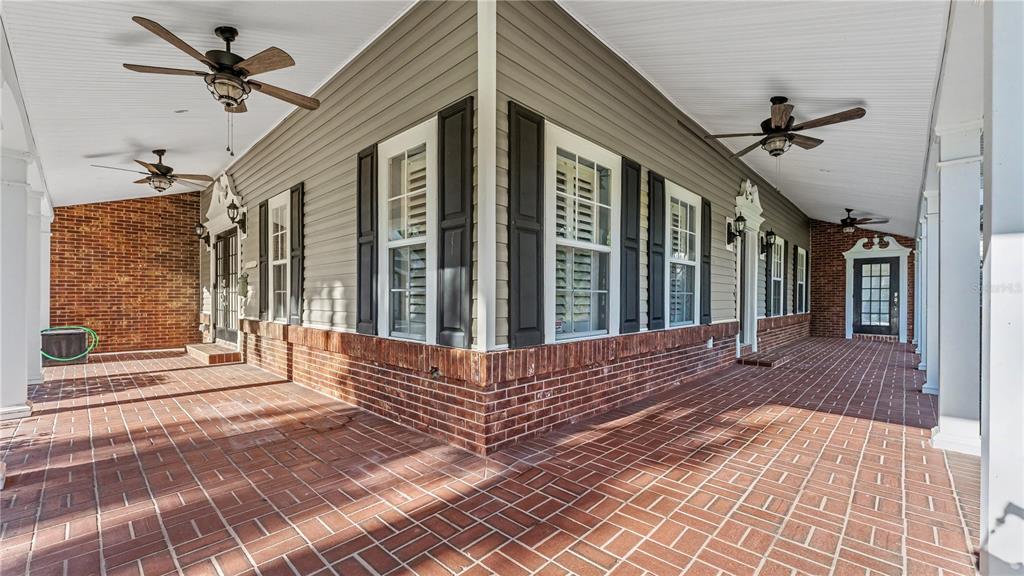 A wide, covered brick porch wraps around the corner of a house with siding — 4233 HOMEWOOD LANE, LAKELAND, FL