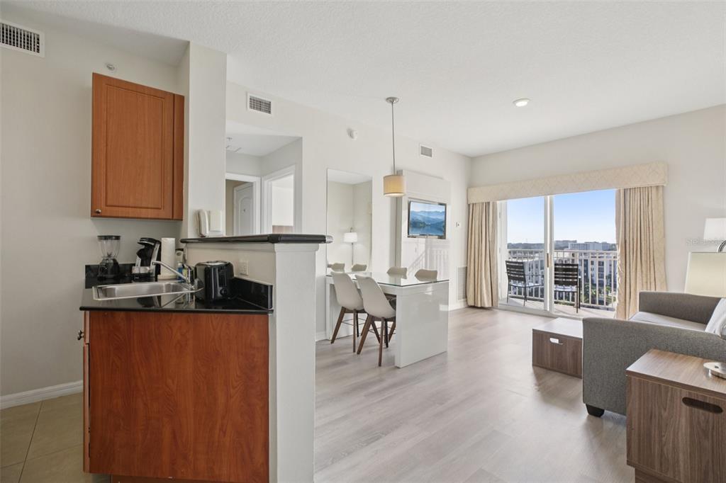 A kitchen with wood cabinets and a dining area leading to a balcony with seating — 7395 UNIVERSAL BOULEVARD UNIT 905, ORLANDO, FL