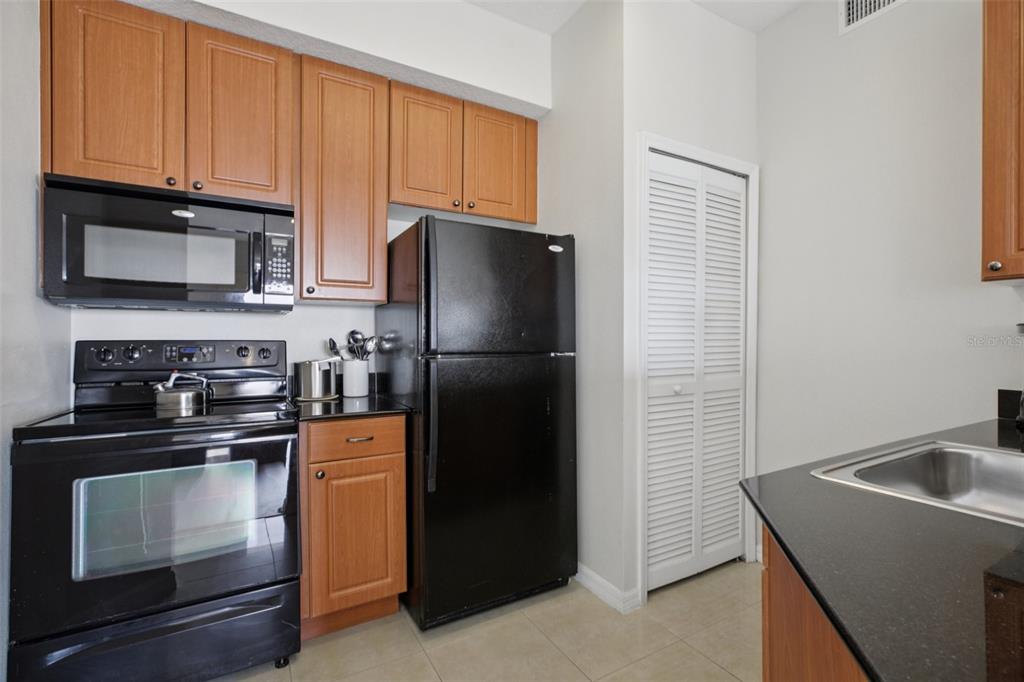 A kitchen features wood cabinets, black appliances, a black countertop, and a white louvered closet door — 7395 UNIVERSAL BOULEVARD UNIT 905, ORLANDO, FL
