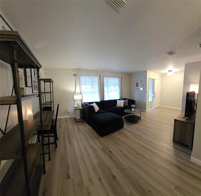A living room features light wood-look flooring, a black sectional sofa, and a metal shelving unit — 819 WALNUT PLACE, ALTAMONTE SPRINGS, FL