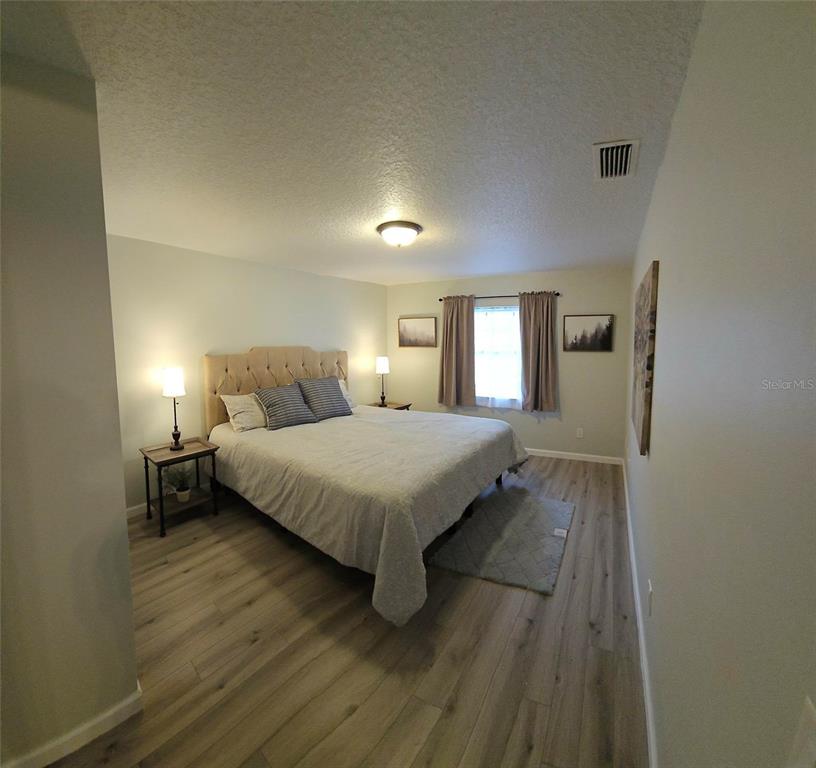 A bedroom features a tufted headboard, light wood-look flooring, and a window with curtains — 819 WALNUT PLACE, ALTAMONTE SPRINGS, FL