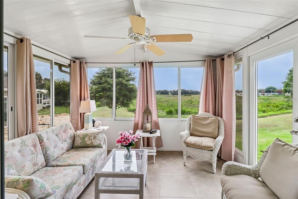 A sunroom with a ceiling fan, wicker furniture, floral sofa, and large windows overlooking greenery — 25120 CLIFFORD HILL, LEESBURG, FL