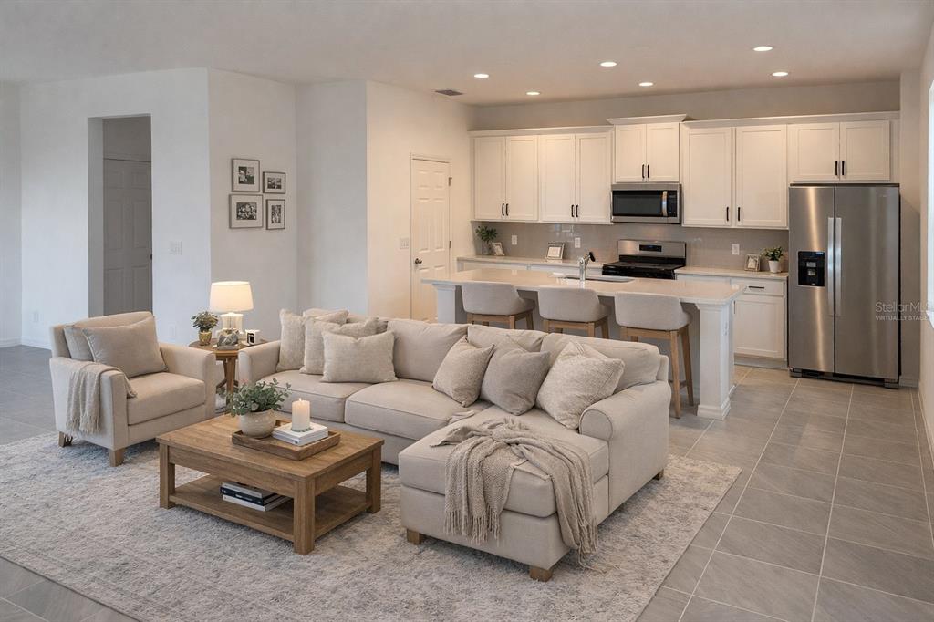 An open-concept kitchen and living room featuring white cabinetry, a kitchen island, and neutral furniture — 6708 SPOTTED EAGLE LOOP, HOWEY IN THE HILLS, FL
