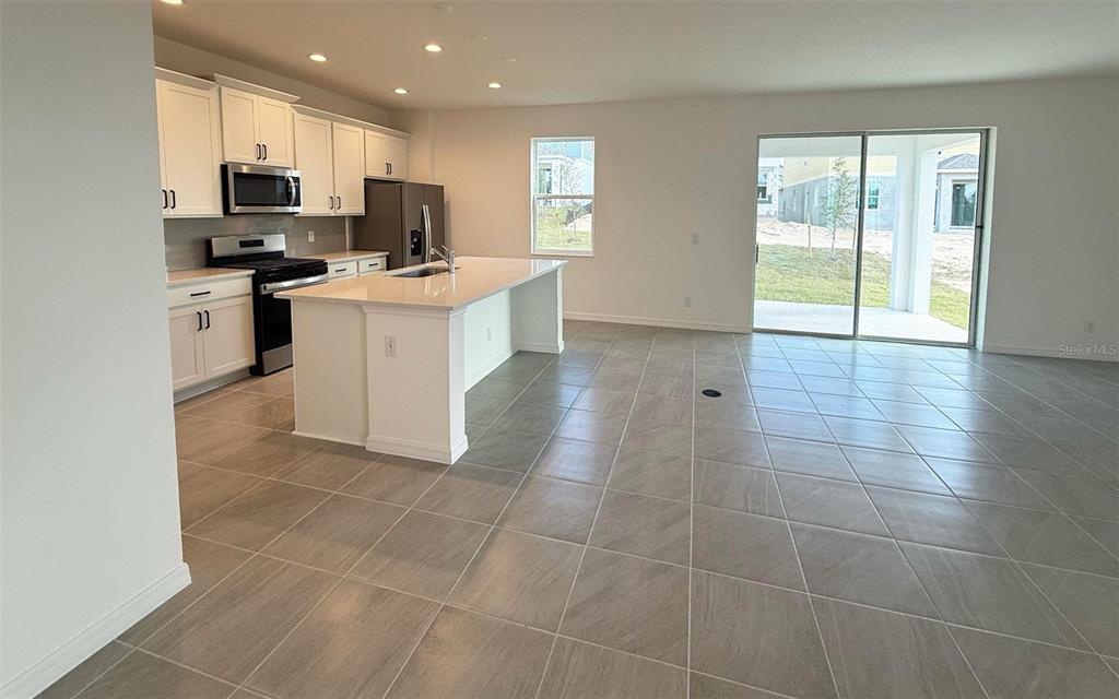 A kitchen with white cabinets, stainless steel appliances, and an island opens to a living area — 6708 SPOTTED EAGLE LOOP, HOWEY IN THE HILLS, FL