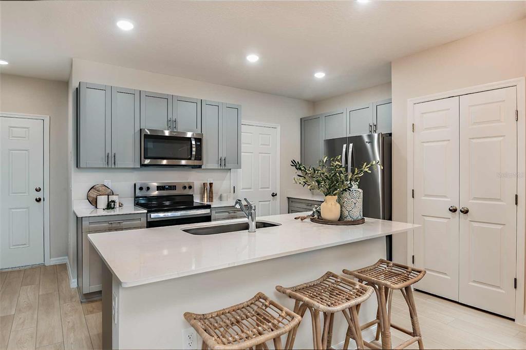 A modern kitchen features gray cabinets, a white quartz island, and three woven bar stools — 4251 HILLOCK BOULEVARD, HAINES CITY, FL