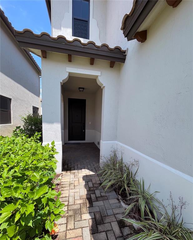 A paved walkway leads to the dark front door of a stucco home with tile accents — 5525 AGOSTINO WAY, AVE MARIA, FL