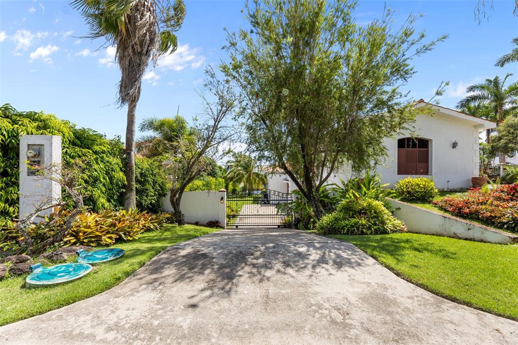 A concrete driveway leads to a gated entrance beside a white house and lush landscaping — Las Vistas 36,  Rio Mar MIRADOR, 36, RIO MAR, RIO GRANDE, PR