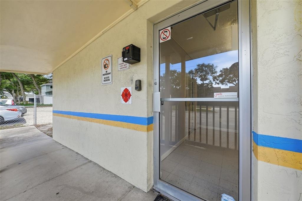A glass door with a security keypad and signage sits on a covered exterior walkway — 2886 WHITNEY ROAD, CLEARWATER, FL
