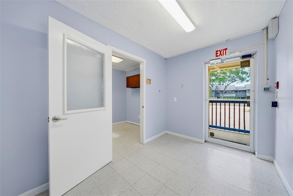 An interior room with light blue walls, white tile flooring, and an exit door — 2886 WHITNEY ROAD, CLEARWATER, FL
