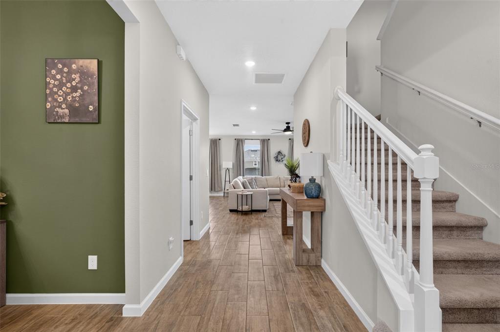 A foyer with wood-look tile flooring leads to a living room past a carpeted staircase — 2340 SIRENA LANE, MOUNT DORA, FL