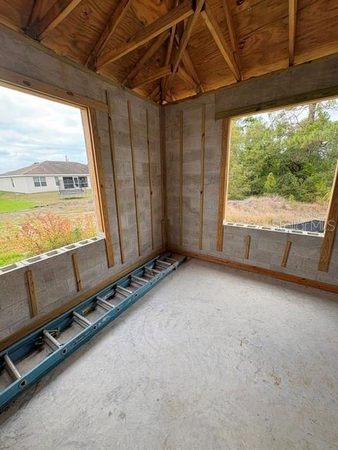 An unfinished room with concrete block walls, exposed wooden rafters, and a blue extension ladder — 3505 39TH STREET SW, LEHIGH ACRES, FL