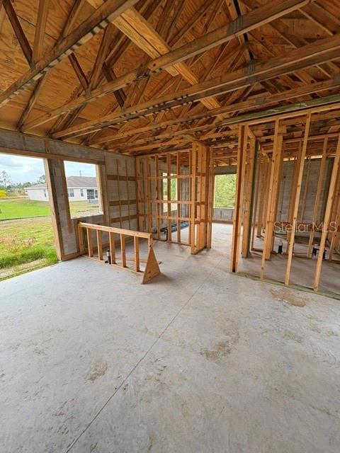 An unfinished room with exposed wooden roof trusses, concrete flooring, and interior wall framing — 3505 39TH STREET SW, LEHIGH ACRES, FL