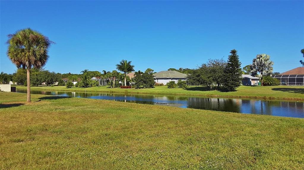 A grassy lawn overlooks a narrow canal with houses and palm trees in the background — 847 ROTONDA CIRCLE, ROTONDA WEST, FL