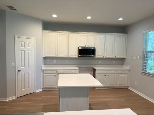 A kitchen features white cabinets, a central island, and light wood-look flooring — 1885 SCRUB JAY RD., APOPKA, FL
