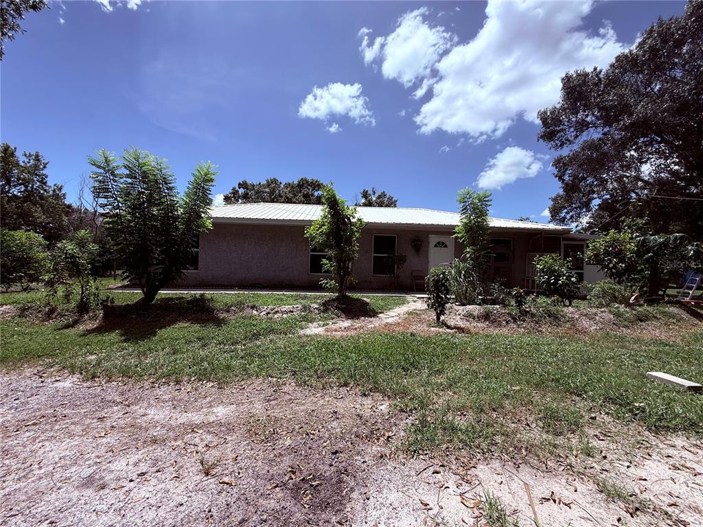 A single-story house with a metal roof sits on a grassy lot with trees — 2015 NW 46TH AVENUE, OKEECHOBEE, FL