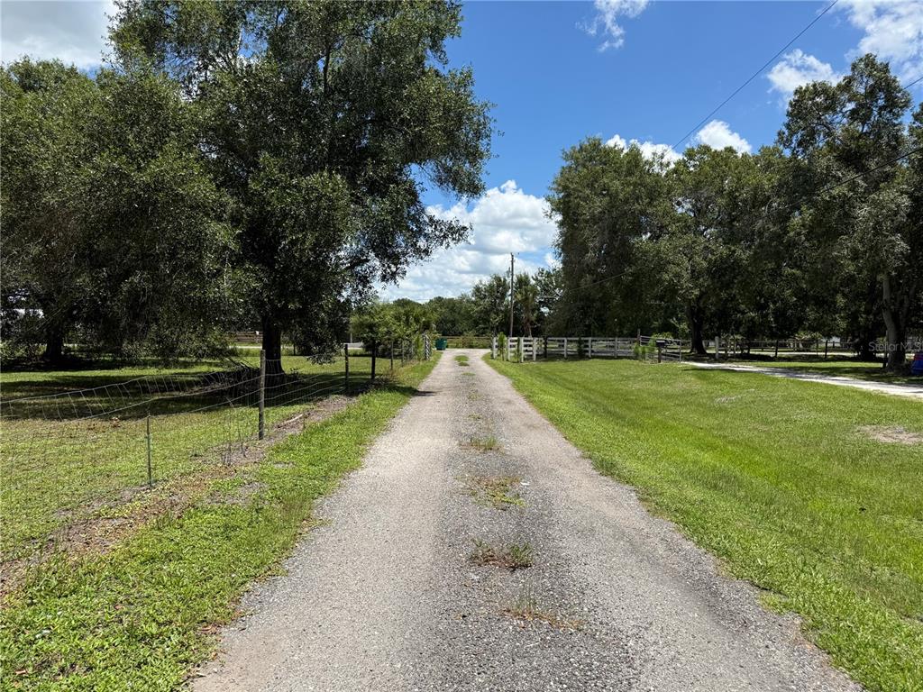 A gravel driveway leads through a grassy property lined with trees and white fencing — 2015 NW 46TH AVENUE, OKEECHOBEE, FL