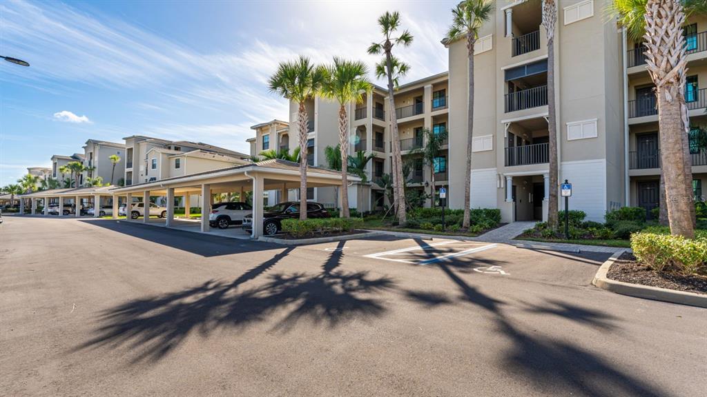 An exterior view of a multi-story apartment building with covered parking and palm trees — 17510 GAWTHROP DRIVE UNIT 105, BRADENTON, FL