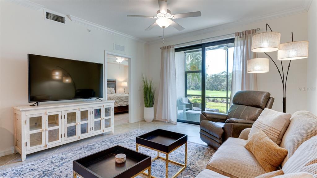 A living room features a large television, a recliner, and a view of a golf course — 17510 GAWTHROP DRIVE UNIT 105, BRADENTON, FL