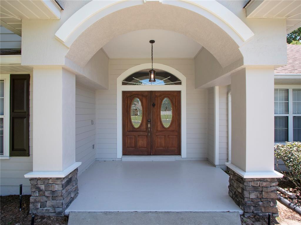 A covered front porch features a double wooden door with oval glass inserts and stone-based columns — 1258 NE 51ST LOOP, OCALA, FL