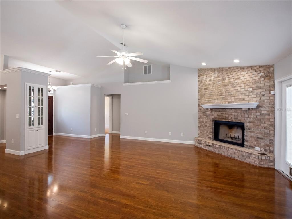 A spacious living room features hardwood floors, a vaulted ceiling, and a brick fireplace — 1258 NE 51ST LOOP, OCALA, FL