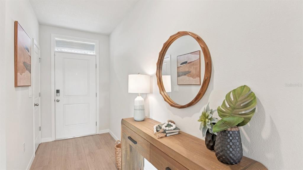 An entryway features a wood console table, a round mirror, and a white front door — 1216 ALPINE ASH PLACE SE, RUSKIN, FL